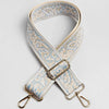 A beige and light blue patterned jacquard strap for a bag, featuring a gold-toned buckle and metal hardware.