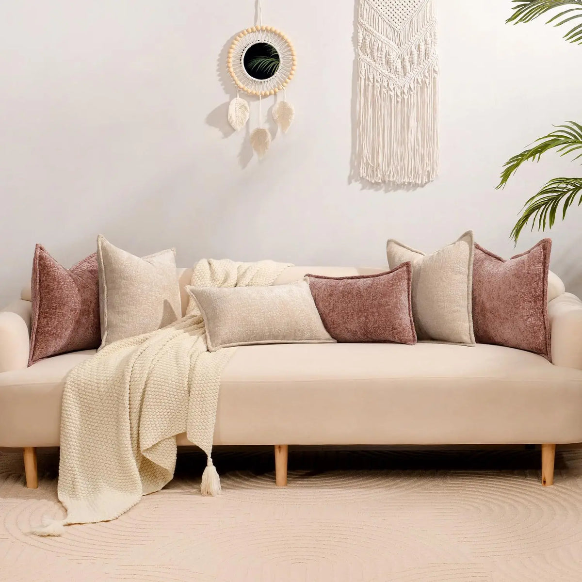 A beige sofa adorned with various textured square throw pillows and a cream knitted throw blanket against a light wall.