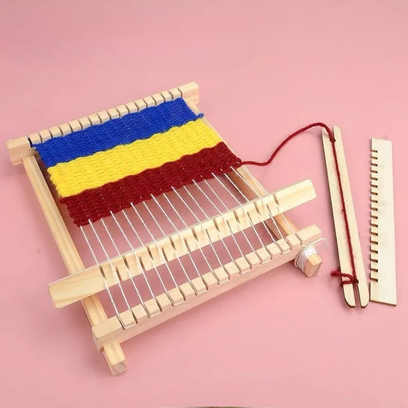 A wooden weaving loom kit with blue, yellow, and red yarn is displayed on a pink background.