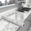 A kitchen countertop with a stainless steel sink and a long marble-patterned roll of vinyl wallpaper.