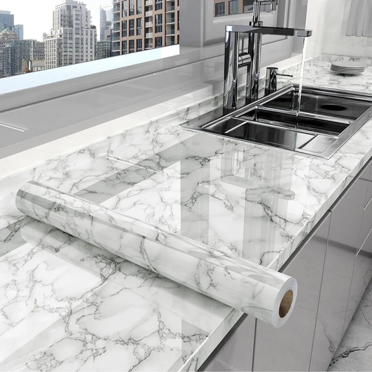 A kitchen countertop with a stainless steel sink and a long marble-patterned roll of vinyl wallpaper.