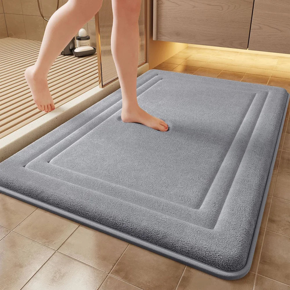 A gray plush memory foam bathroom mat is placed on a tiled floor next to a shower area.
