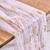 Pink tulle table runner with delicate floral embroidery draped over a wooden table.