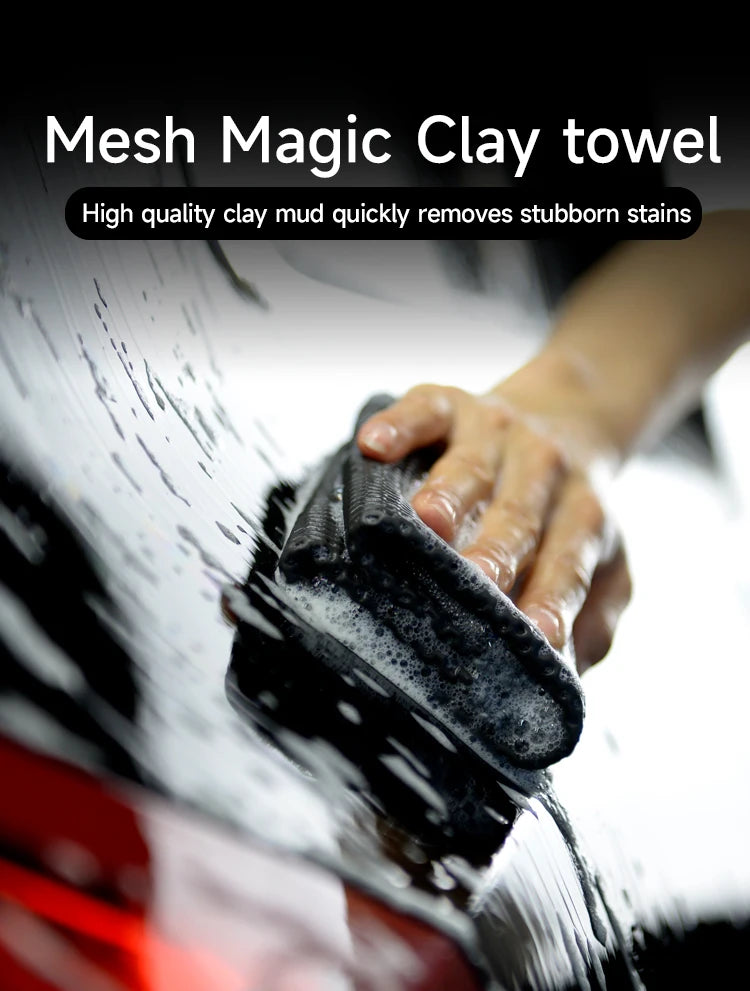 A hand is using a black mesh clay towel to clean mud stains from a car's paint surface.