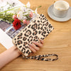 A hand holds a leopard print retro long wallet on a wooden table next to a cup and some flowers.