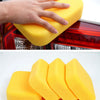 A hand is using a yellow high-density car wash sponge on a car's taillight, next to several yellow sponges.