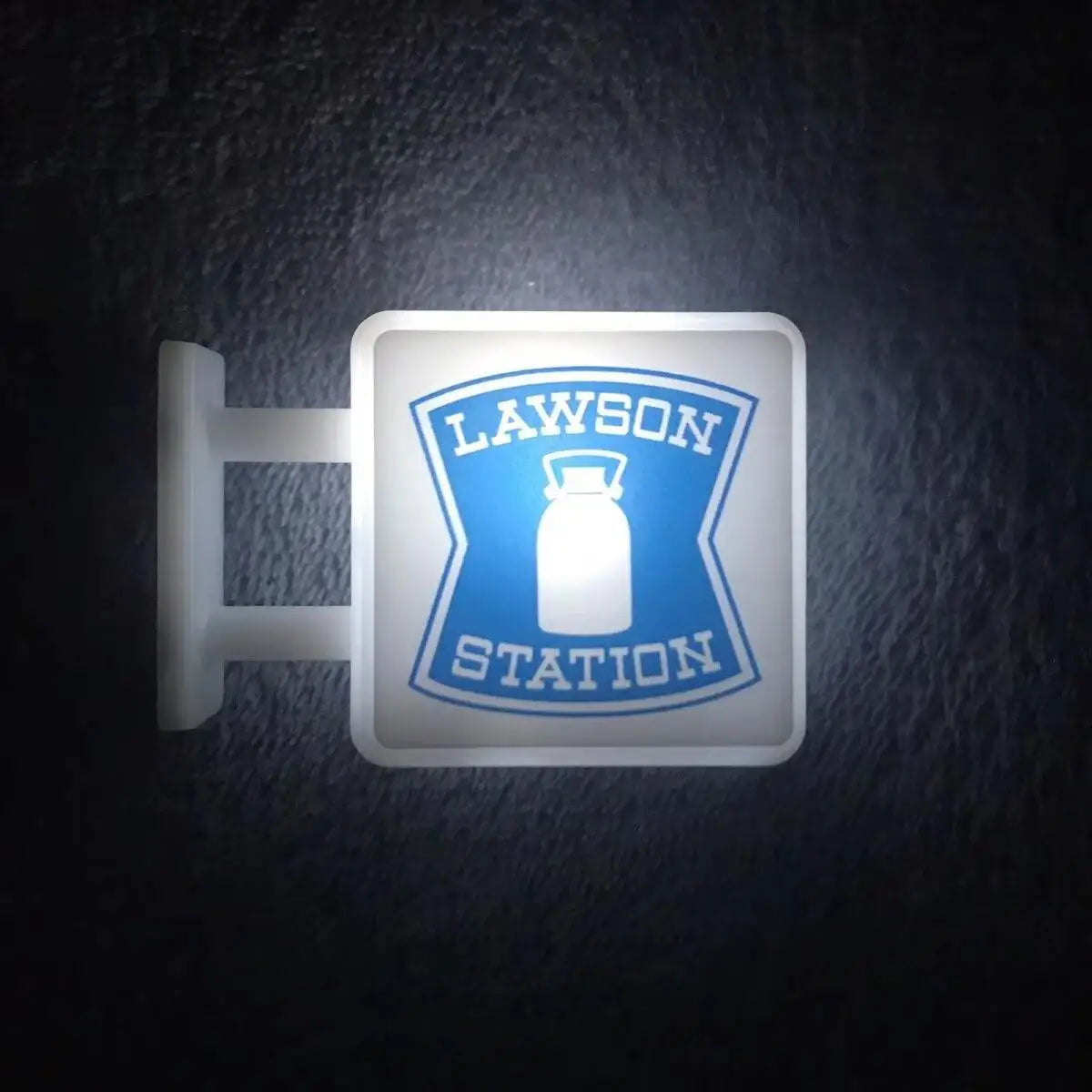 A white rectangular magnet featuring the Lawson station logo and a bottle design, illuminated by a night light.