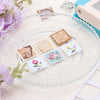 A clear glass plate holds several square postage stamp paper punches for crafting and scrapbooking