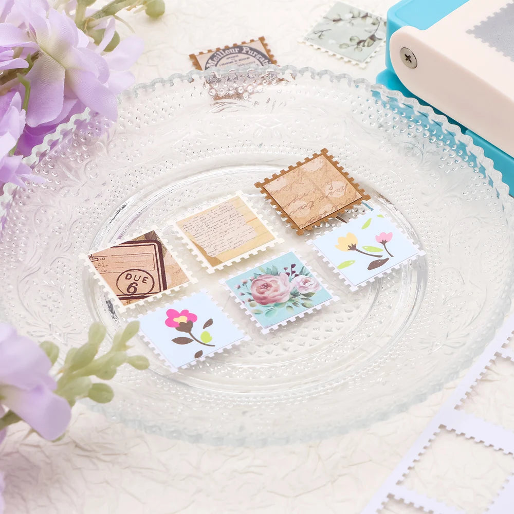 A clear glass plate holds several square postage stamp paper punches for crafting and scrapbooking