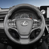 A close-up view of a black steering wheel with a carbon fiber texture cover and controls inside a car interior.