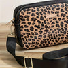 A black and tan leopard print crossbody bag with a gold hardware strap resting on a wooden surface.
