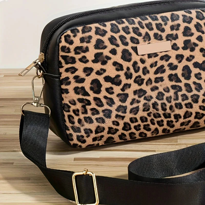 A black and tan leopard print crossbody bag with a gold hardware strap resting on a wooden surface.