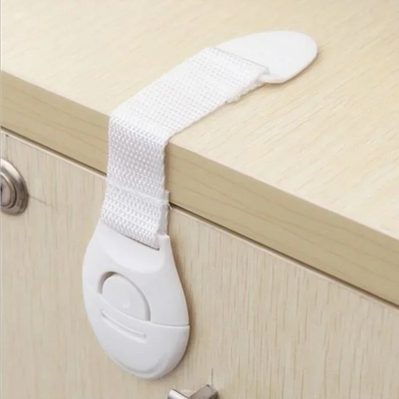 White multi-purpose baby safety strap attached to a cabinet drawer handle.