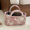 A pink quilted fabric storage basket with a handle and floral pattern sits on a white surface.