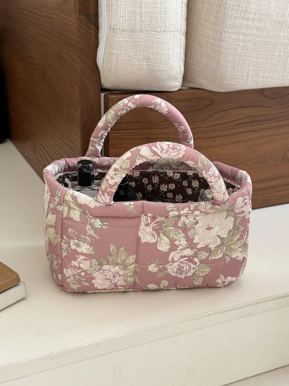 A pink quilted fabric storage basket with a handle and floral pattern sits on a white surface.