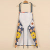 A white kitchen apron with a floral print featuring yellow and blue daisies, hanging on a wooden hanger.