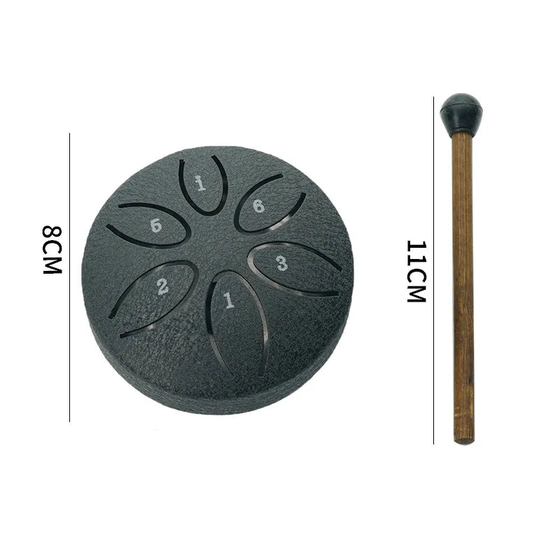 A black mini steel tongue drum with six tuning holes and a wooden mallet shown next to a measurement scale.