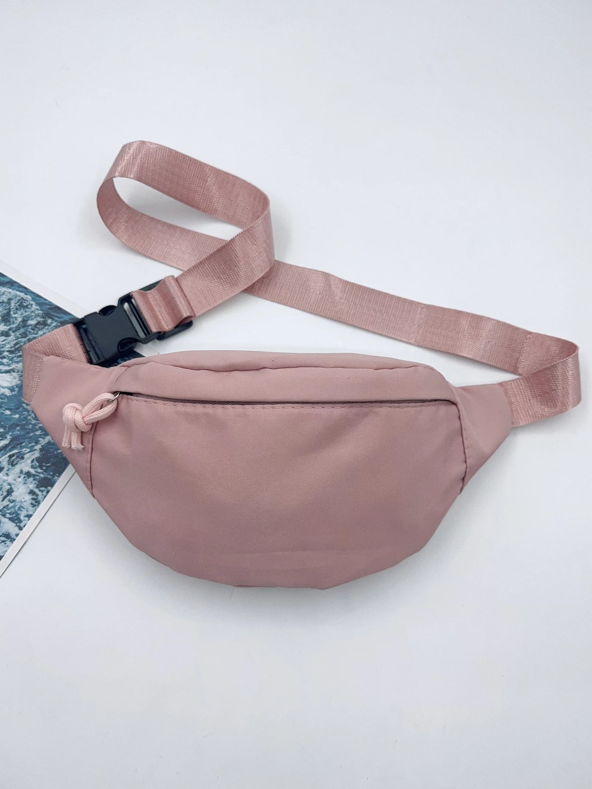 Bolso cruz de nylon rosa claro con correa y un pequeño borla rosa contra fondo blanco.