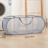 A gray folding mesh laundry basket with handles is shown on a light wooden floor.