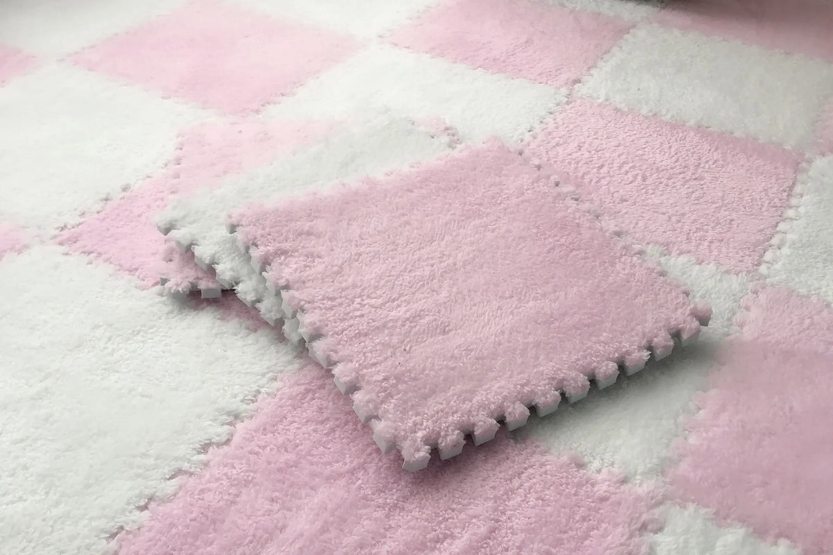 A square pink plush tile resting on a pink and white checkered rug.