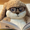 A fluffy brown rabbit plush toy wearing dark glasses looking at an open book.