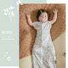A baby wearing a light green and white patterned vest sleeping bag on a brown textured surface.