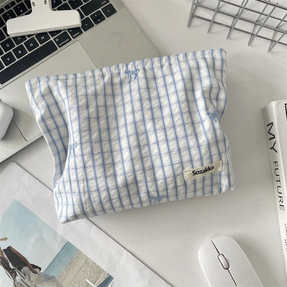 A light blue and white striped fabric makeup bag with floral embroidery resting on a white surface.