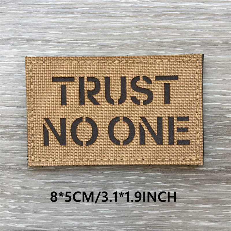 A rectangular tan fabric patch with the text TRUST NO ONE printed in black block letters on a weathered wooden surface.