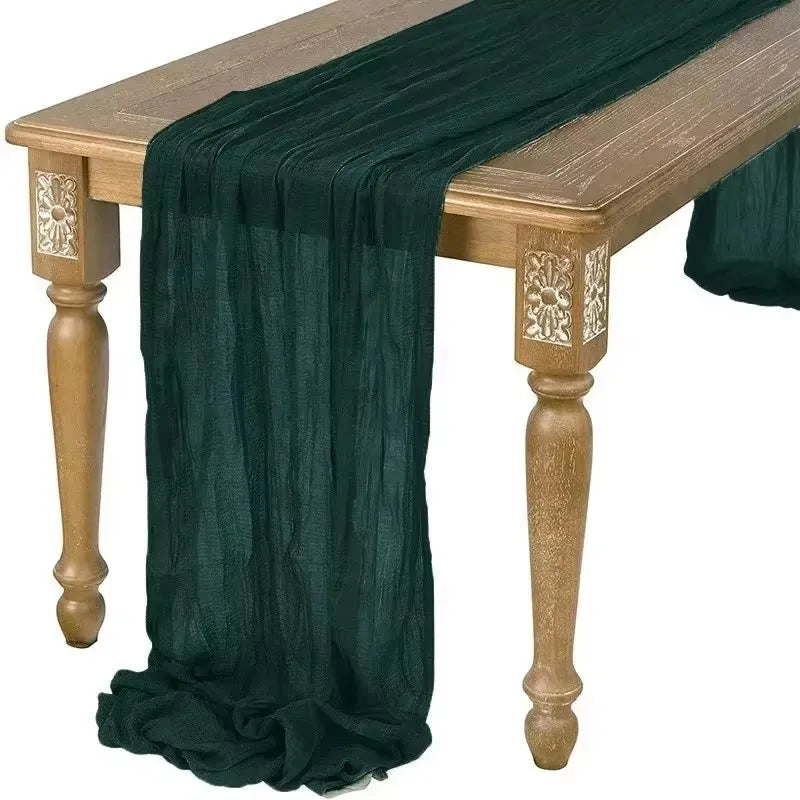 Dark green cotton gauze table runner draped over a rustic wooden table.