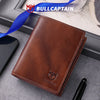 A brown genuine leather men's bifold wallet with stitching is shown next to a blue ribbon and a black pen.