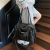 A woman holds a black soft leather plaid crossbody bag with an adjustable strap on a wooden staircase.