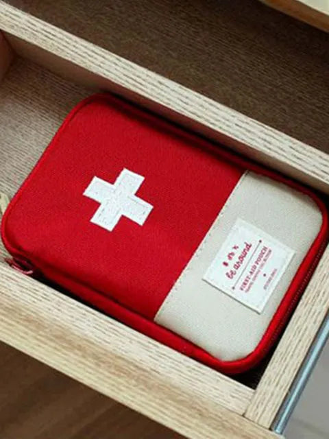 A red and white compact travel medicine organizer bag is placed inside a light wood box.