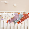 A baby sensory tag comfort blanket with a soothing teether hanging on a white crib railing.
