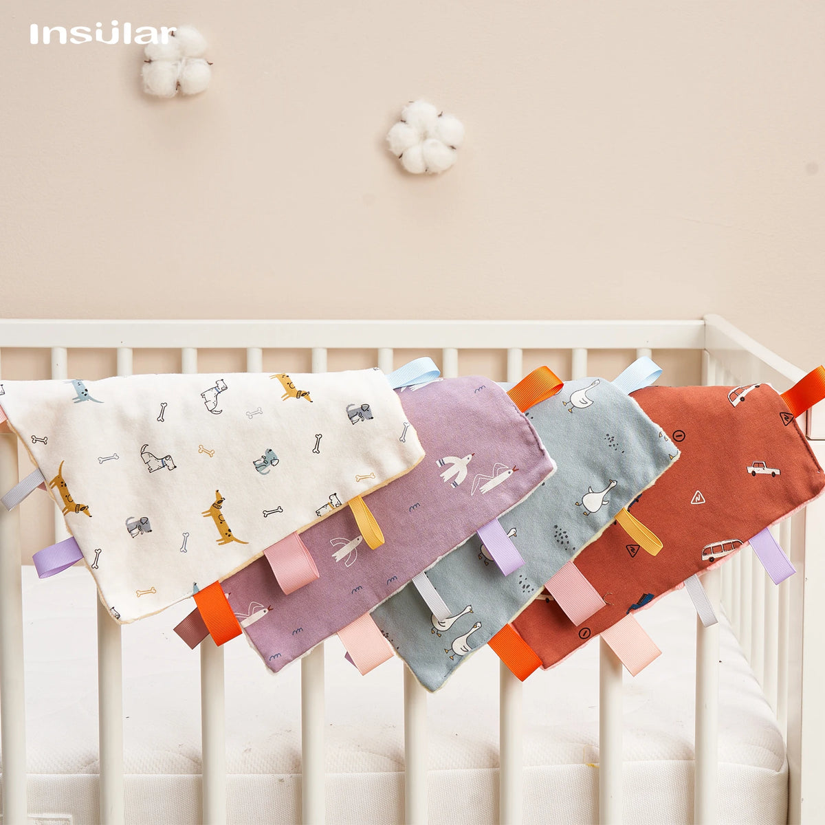 A baby sensory tag comfort blanket with a soothing teether hanging on a white crib railing.