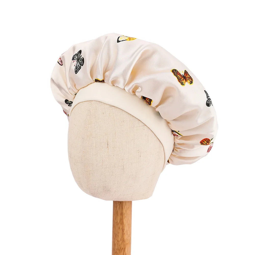 A light beige satin sleep cap for kids featuring a butterfly print, displayed on a headless mannequin.
