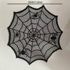 A black, intricate spider web design on a clear mesh material used as a Halloween table runner or placemat.