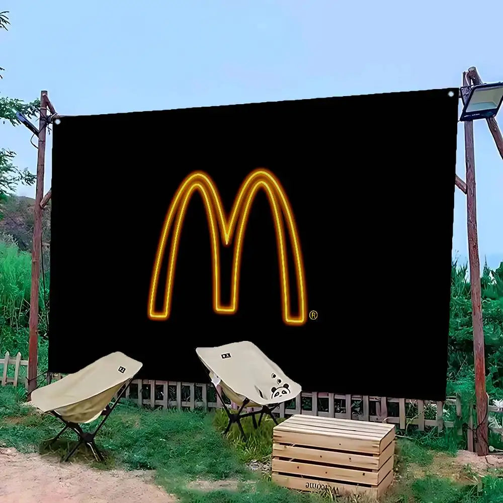 Une bannière noire avec le logo 'M' de McDonald's jaune brillant, en extérieur avec de la verdure et des palettes en bois.