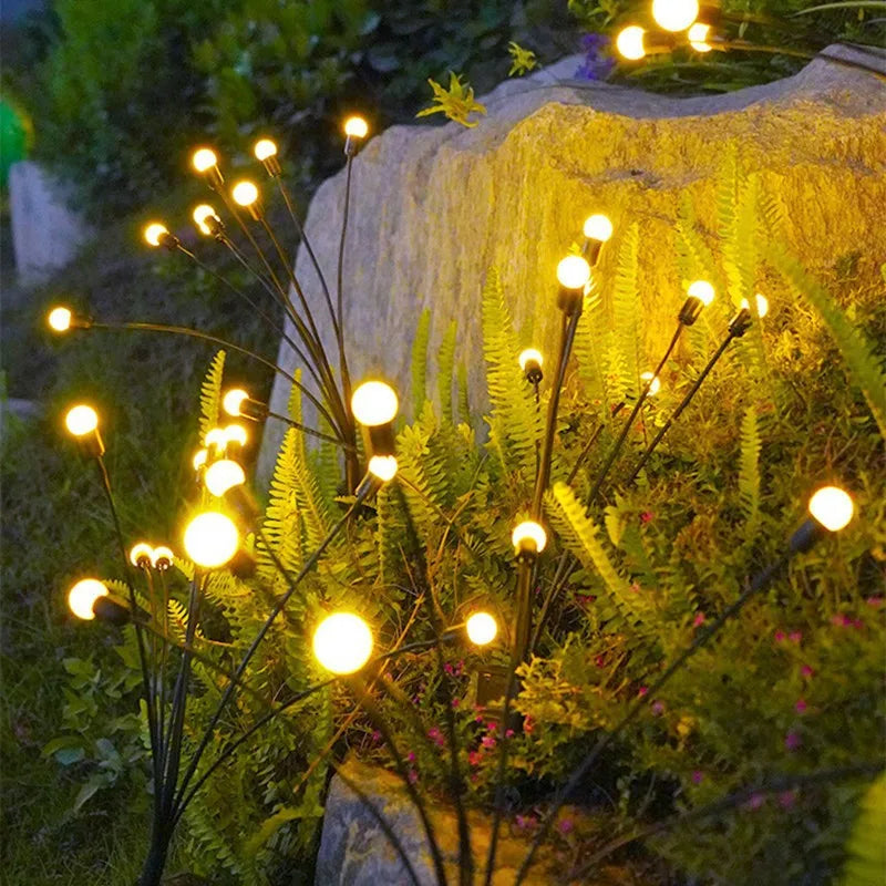 Nahaufnahme von solarbetriebenen Glühwürmchen-Gartenlichtern, die grünes Laub am Abend beleuchten.