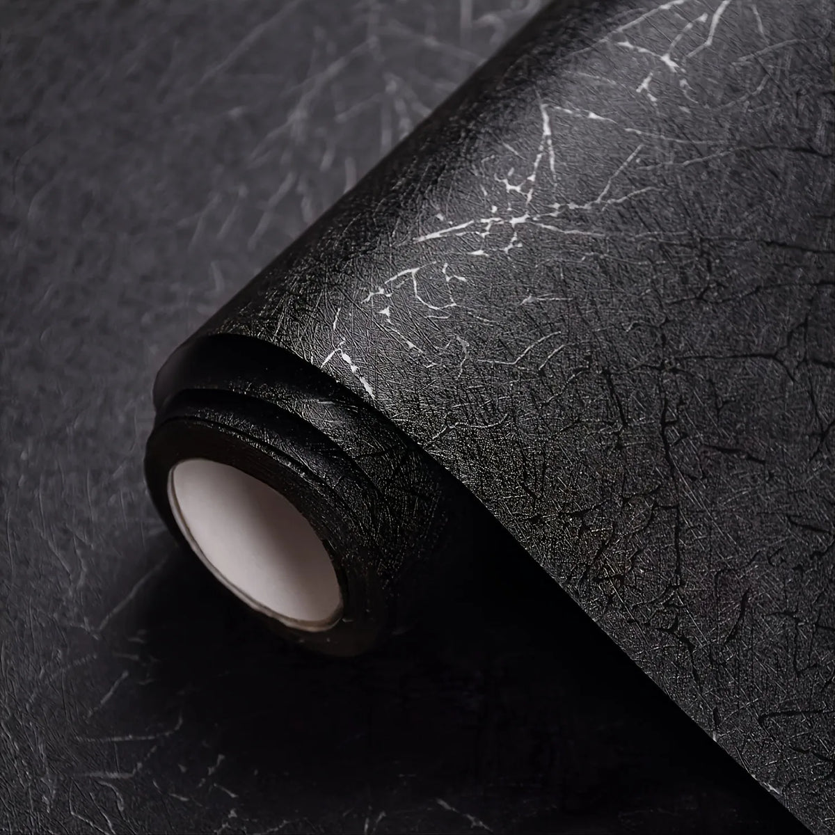 Roll of black textured self-adhesive wallpaper with visible crackle effects