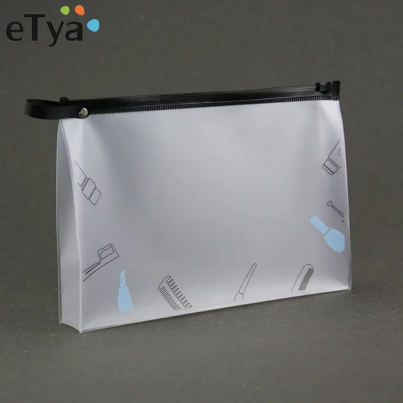 A transparent travel toiletry bag with a black zipper and hanging hooks is shown against a gray background.