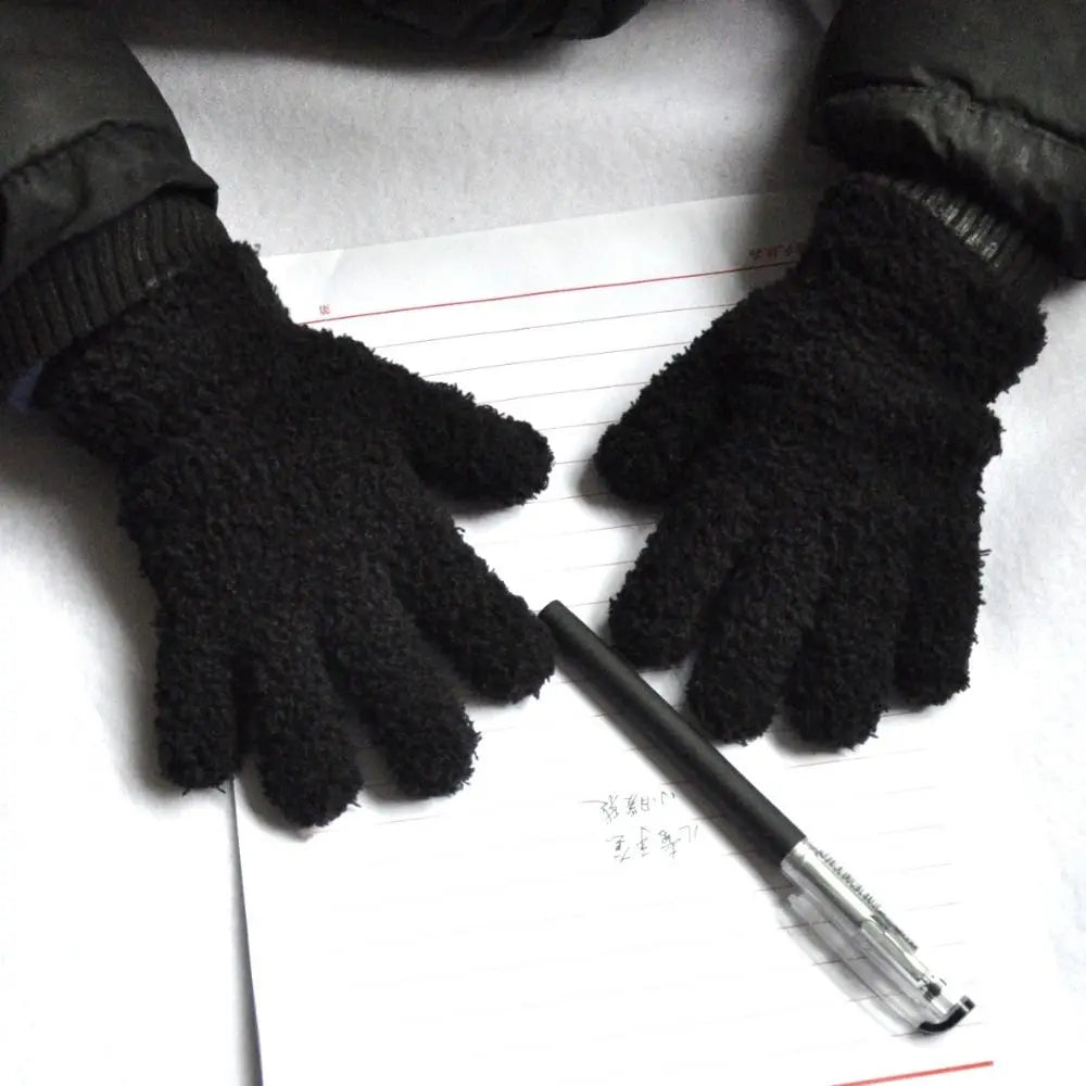 A pair of black fuzzy winter gloves resting on a piece of lined paper.