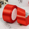 A roll of bright red satin ribbon for gift wrapping and crafts lying on a white surface.