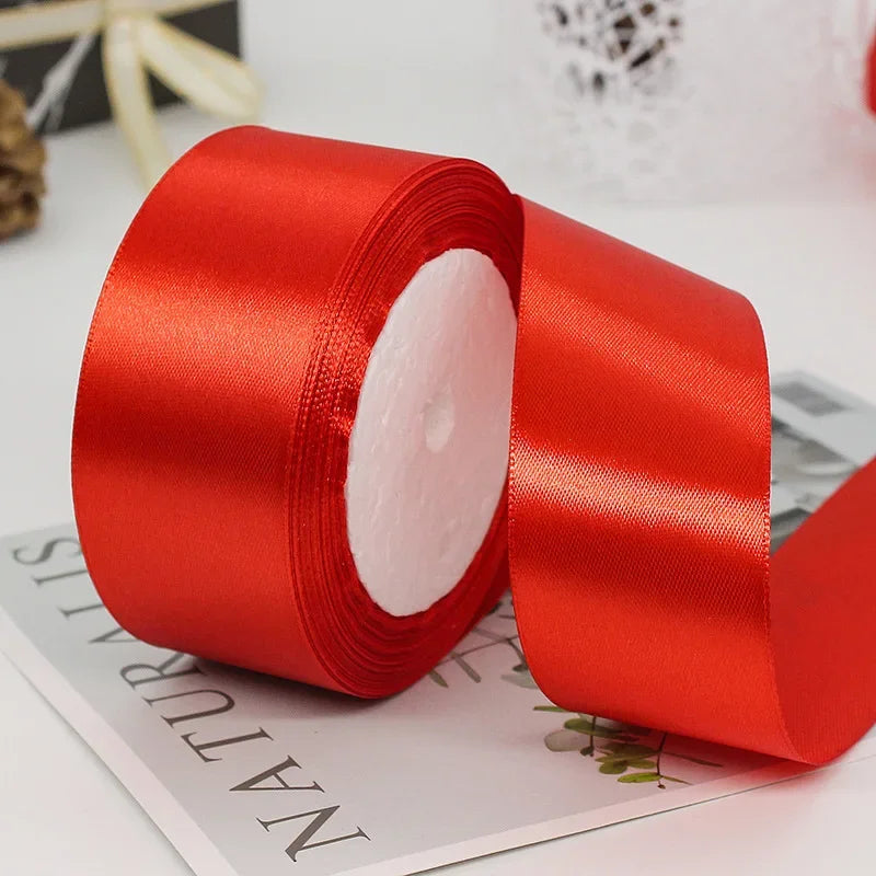 A roll of bright red satin ribbon for gift wrapping and crafts lying on a white surface.