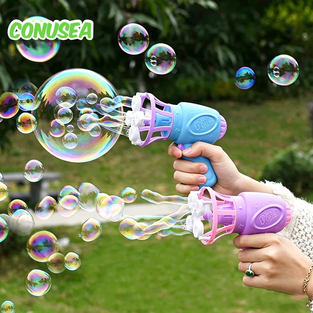 A hand is using a purple automatic bubble gun to blow bubbles into the air in a green outdoor setting.