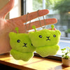 A hand holds two bright lime green alien plush keychains with black eyes and small ears.