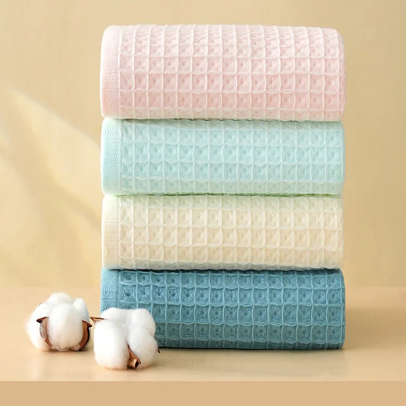 A stack of four rectangular waffle weave bath towels in pink, light blue, cream, and deep blue colors with fluffy white cotto