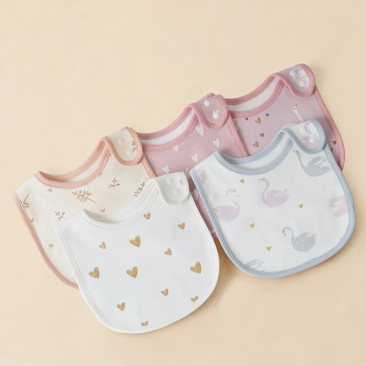 A set of pink and white cotton baby bibs with a U-shaped design featuring small heart and swan patterns.