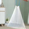 A sheer white drawstring trash bag with blue handles hanging, displayed next to a white cabinet and potted plant.