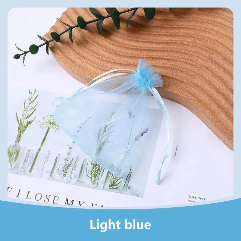 Light blue organza drawstring jewelry gift bags with dried herbs displayed on a wooden surface.