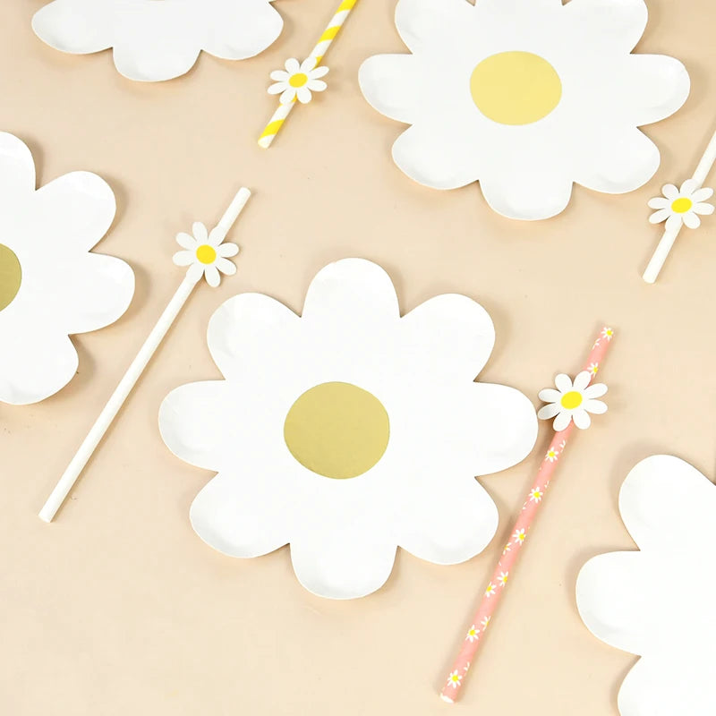 A collection of white daisy flower shaped disposable party tableware, including plates and sticks.